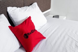 Una cama con ropa de cama blanca y una almohada roja con un logotipo.
