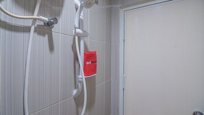 Une douche avec une serviette rouge accrochée au mur, une porte sur la droite et un mur recouvert de carreaux.