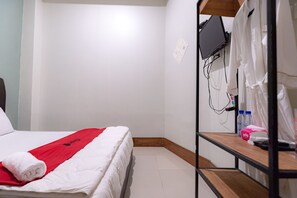 A hotel room with a bed, a red towel, a TV mounted on the wall, and a shelf with toiletries. - RedDoorz near Hang Nadim Batam Airport (Batam)