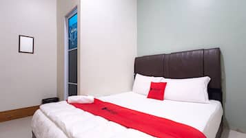 A hotel room with a large bed, white bedding, a red throw blanket, and a brown headboard.