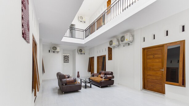 A spacious living area with two sofas, a coffee table, and a wooden door. - RedDoorz near Pascasarjana UGM 2 (Pogung Lor)