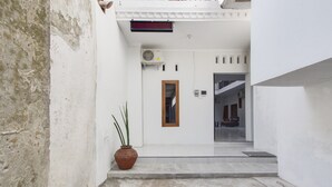 A narrow hallway with a potted plant, a door with a small window, and a staircase leading to another level. - RedDoorz near Pascasarjana UGM 2 (Pogung Lor)