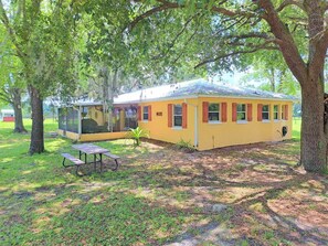 Een geel huis met rode luiken, een overdekte veranda en een picknicktafel in een bebost gebied.