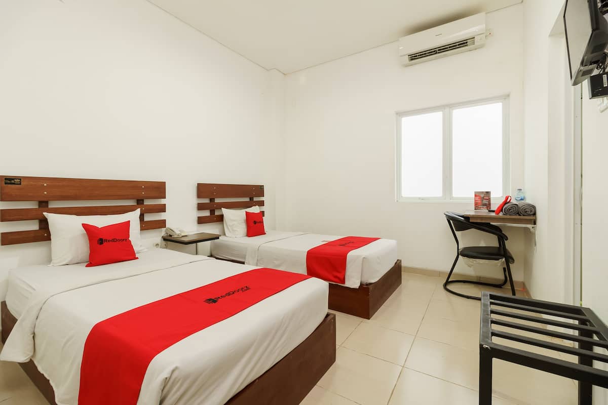 A hotel room with two beds, a desk, a chair, and a window.