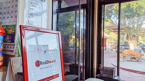 Ein RedDoorz Schild, ein Kalender und ein Blick durchs Fenster auf eine Terrasse mit Außenbestuhlung.