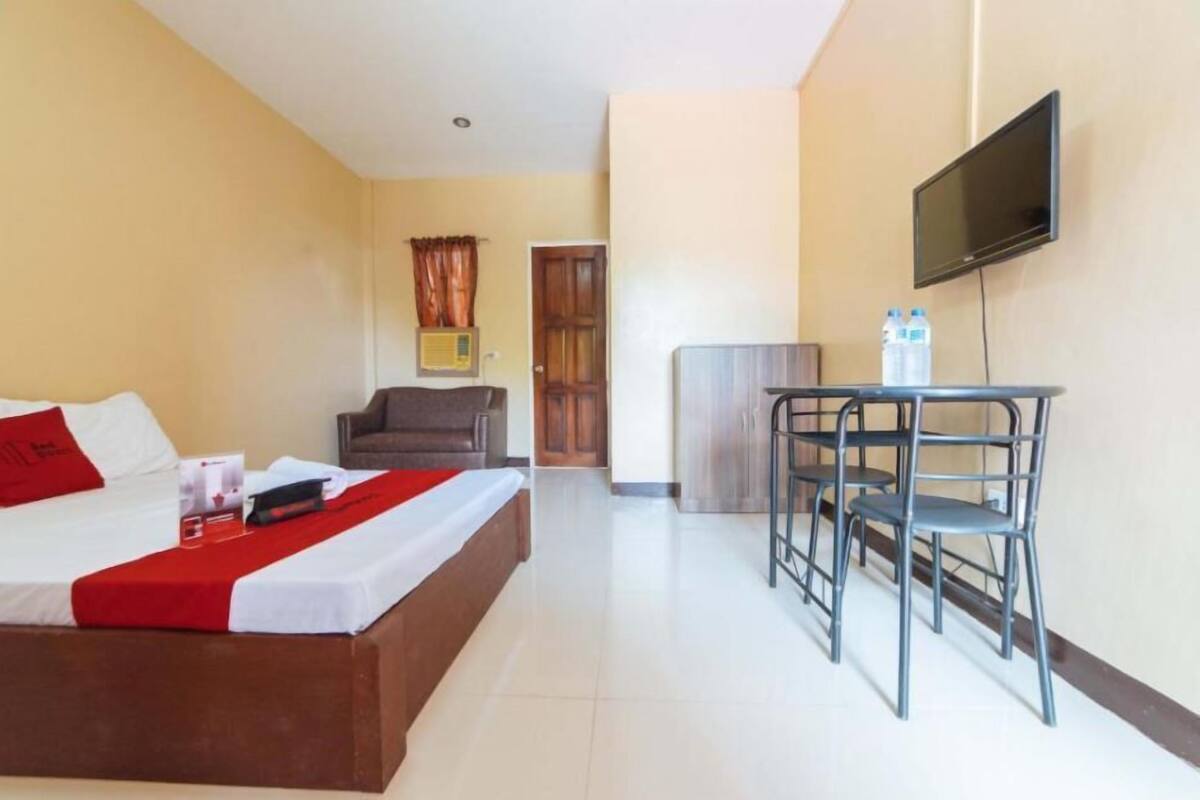 Une chambre d’hôtel comprenant un lit, un bureau avec des chaises, une télévision et une porte donnant sur une autre pièce.