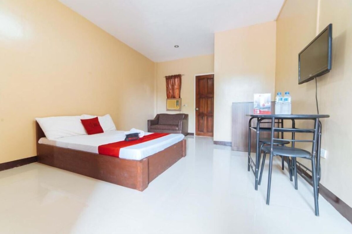 A hotel room with a bed, a desk with chairs, a television, and a refrigerator.