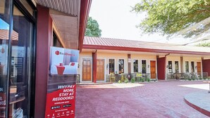 Ein RedDoorz Schild vor einem Gebäude mit rotem Dach und einer überdachten Terrasse.