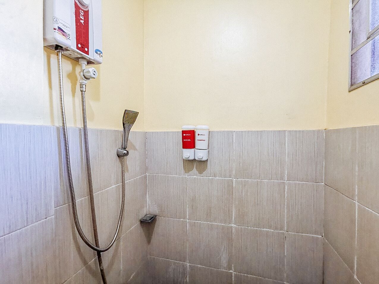 A shower area with a handheld showerhead, a wall-mounted faucet, and two soap dispensers.