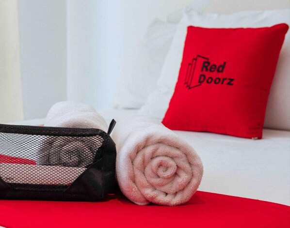 A neatly made bed with a red pillow labeled "Red Doorz" and a black mesh bag with a rolled-up towel. - RedDoorz Plus near Dadiangas Heights (General Santos)