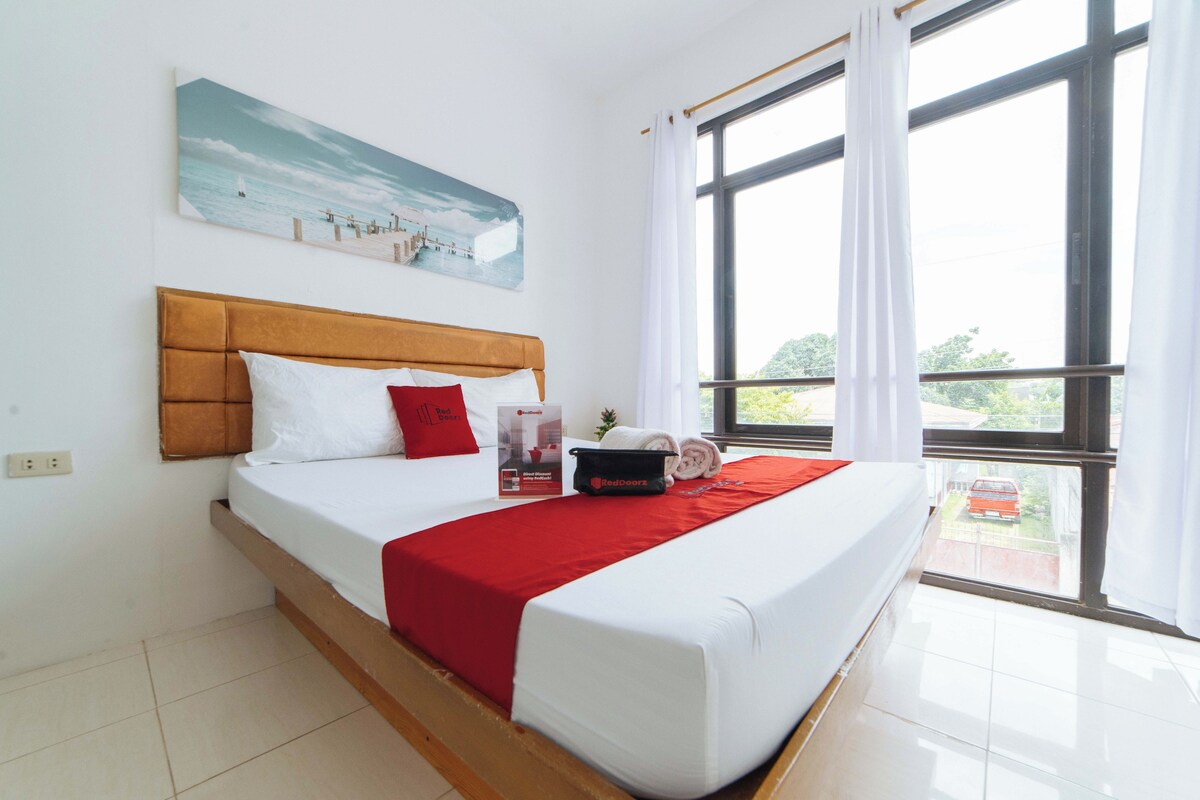 A hotel room with a bed, a painting, a window with curtains, and a view of the outside.
