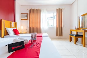 Ein Hotelzimmer mit zwei Betten, einem Schreibtisch, einem Stuhl, einer Lampe, einem Fenster mit Vorhängen und einer RedDoorz Strandtasche.