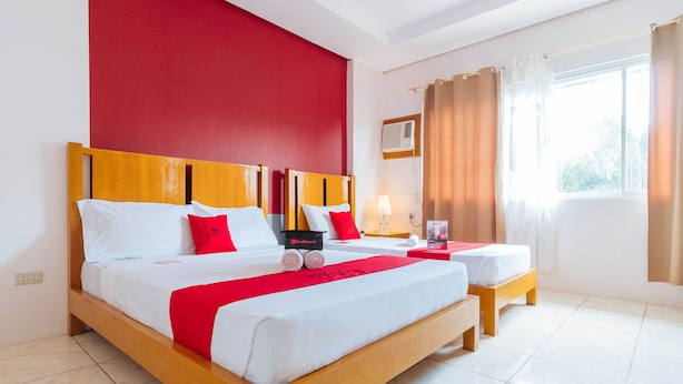 A hotel room with a large bed, two bedside tables, a red accent wall, a window with curtains, and a ceiling fan. - RedDoorz near Caticlan Airport (Malay)