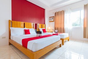 Una habitación de hotel con una cama grande, dos mesitas de noche, una pared de acento roja, un ventanal con cortinas y un ventilador de techo.