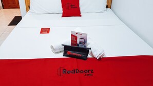 Un letto rifatto con cura, un cuscino rosso, una brochure RedDoorz e un asciugamano.