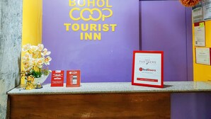 Una reception con una parete viola, una insegna che recita 'BOHOL COOP TOURIST INN' e un cartello RedDoorz Partners.
