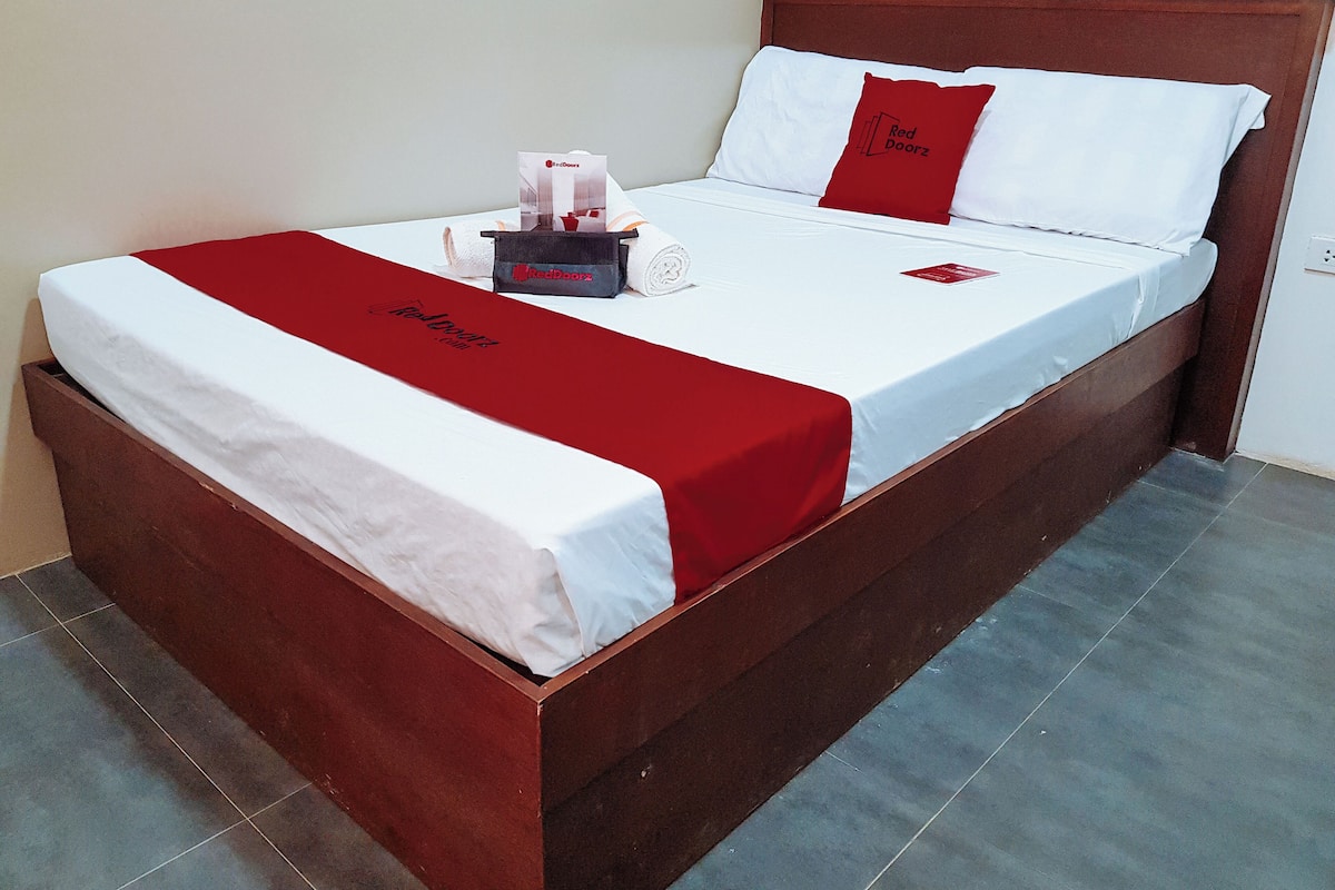 A neatly made bed with a red and white bedspread, a red pillow, and a red door sign on the headboard.