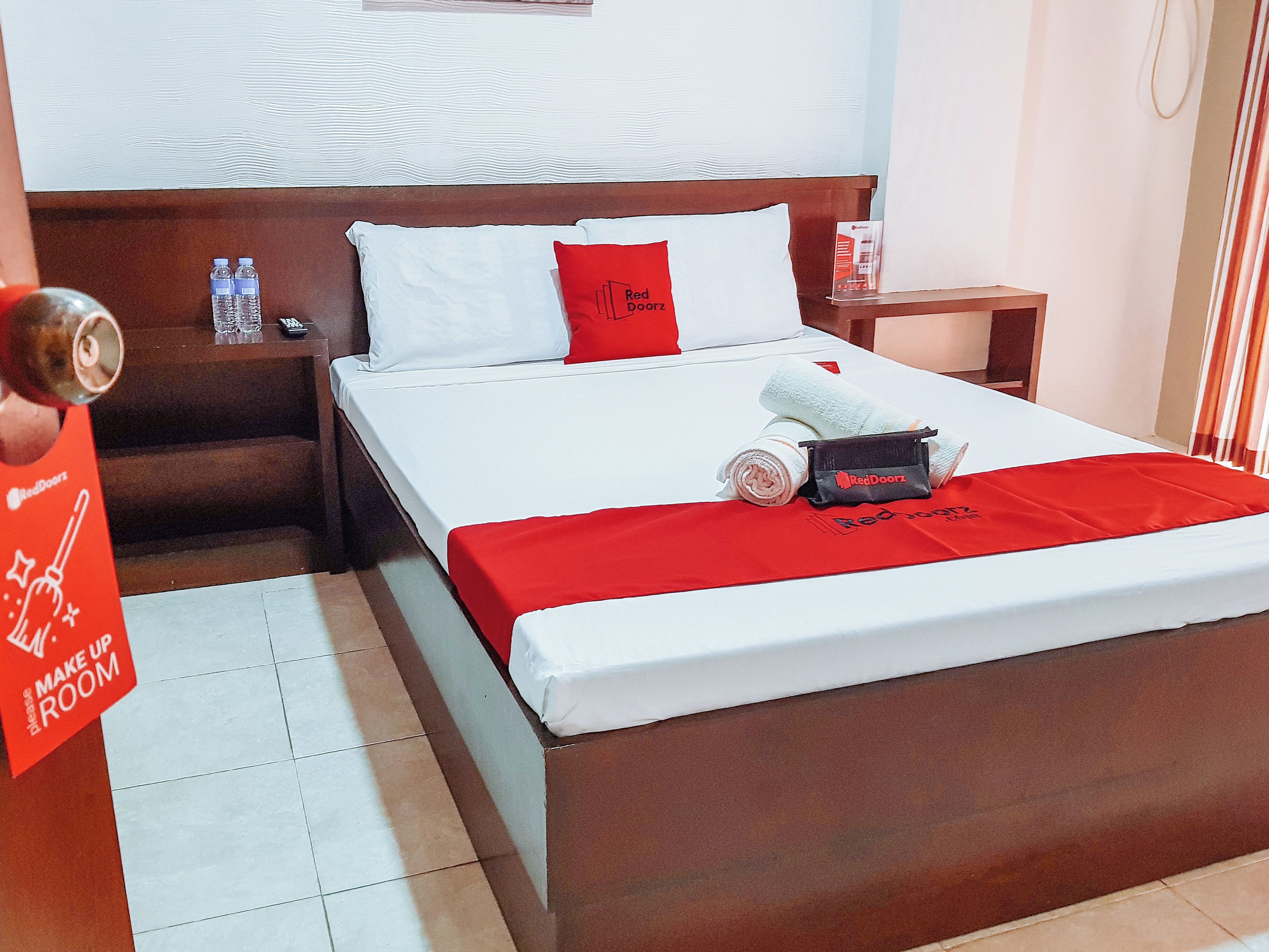 Una habitació d'hotel amb llit, almoines, una tauleta de nit, una tovallola vermella i un cartell de RedDoorz.