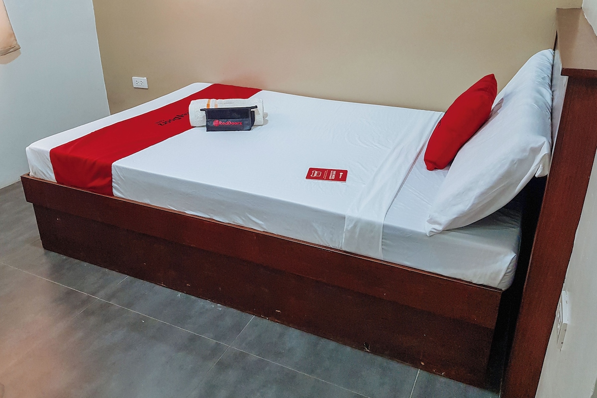 A single bed with a red and white bedspread, a pillow, a red tag, and a small item on the bed.
