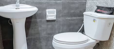 A bathroom with a pedestal sink, toilet, and a small white box on the wall.