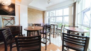 A modern dining area with round tables and dark wooden chairs, large windows offering a view, and a ceiling fan. - RedDoorz @ Lawaan Roxas City (Roxas City)