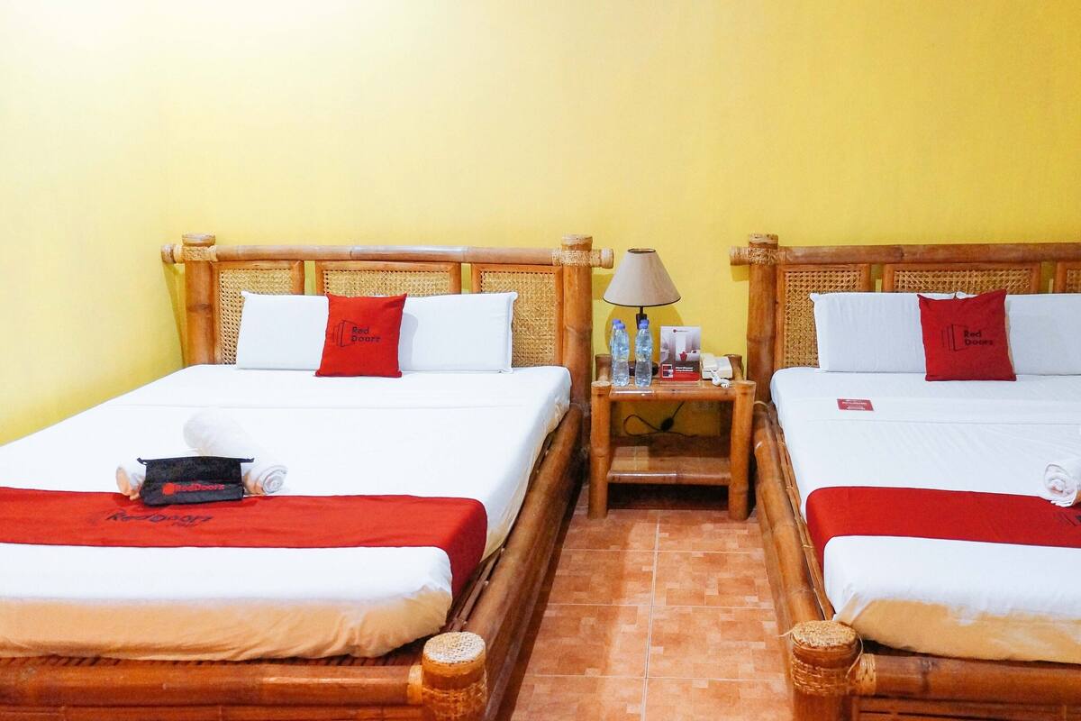 Two beds with red bedding, a nightstand with a lamp and water bottles, and a red pillow with the Red Doorz logo.