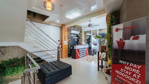 A hotel lobby with a staircase, a reception desk, and a RedDoorz advertisement. - RedDoorz @ Lawaan Roxas City (Roxas City)