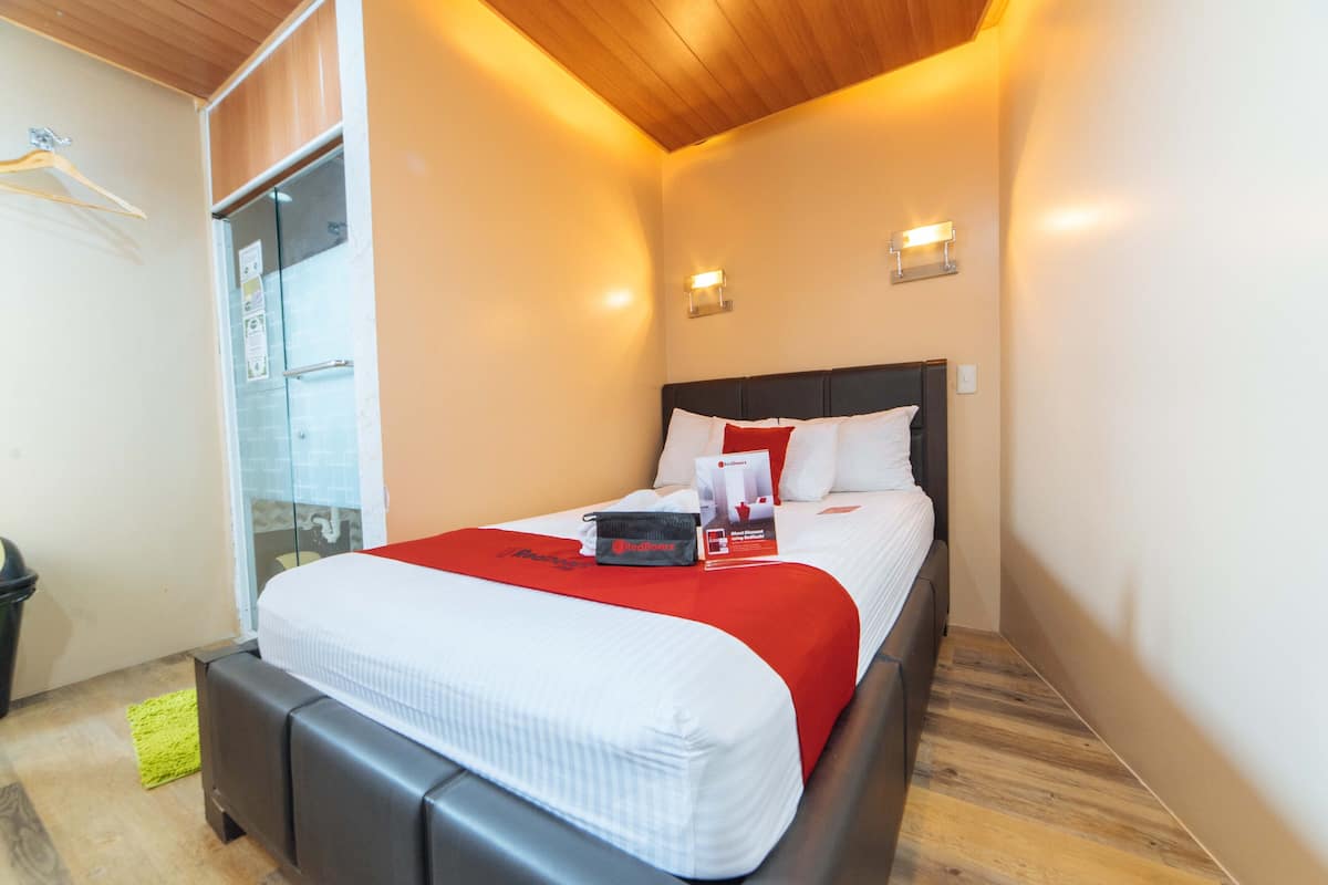 A hotel room with a bed, a bedside table, a hanging coat rack, and a glass door leading to a balcony.