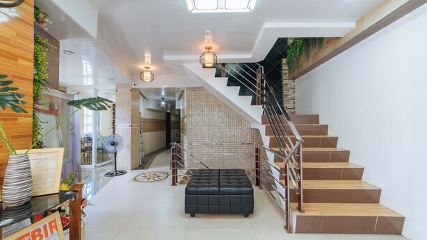 A modern interior with a staircase, a black leather ottoman, and a reception area with a 'SKIP FOR RECEIPT' sign. - RedDoorz @ Lawaan Roxas City (Roxas City)