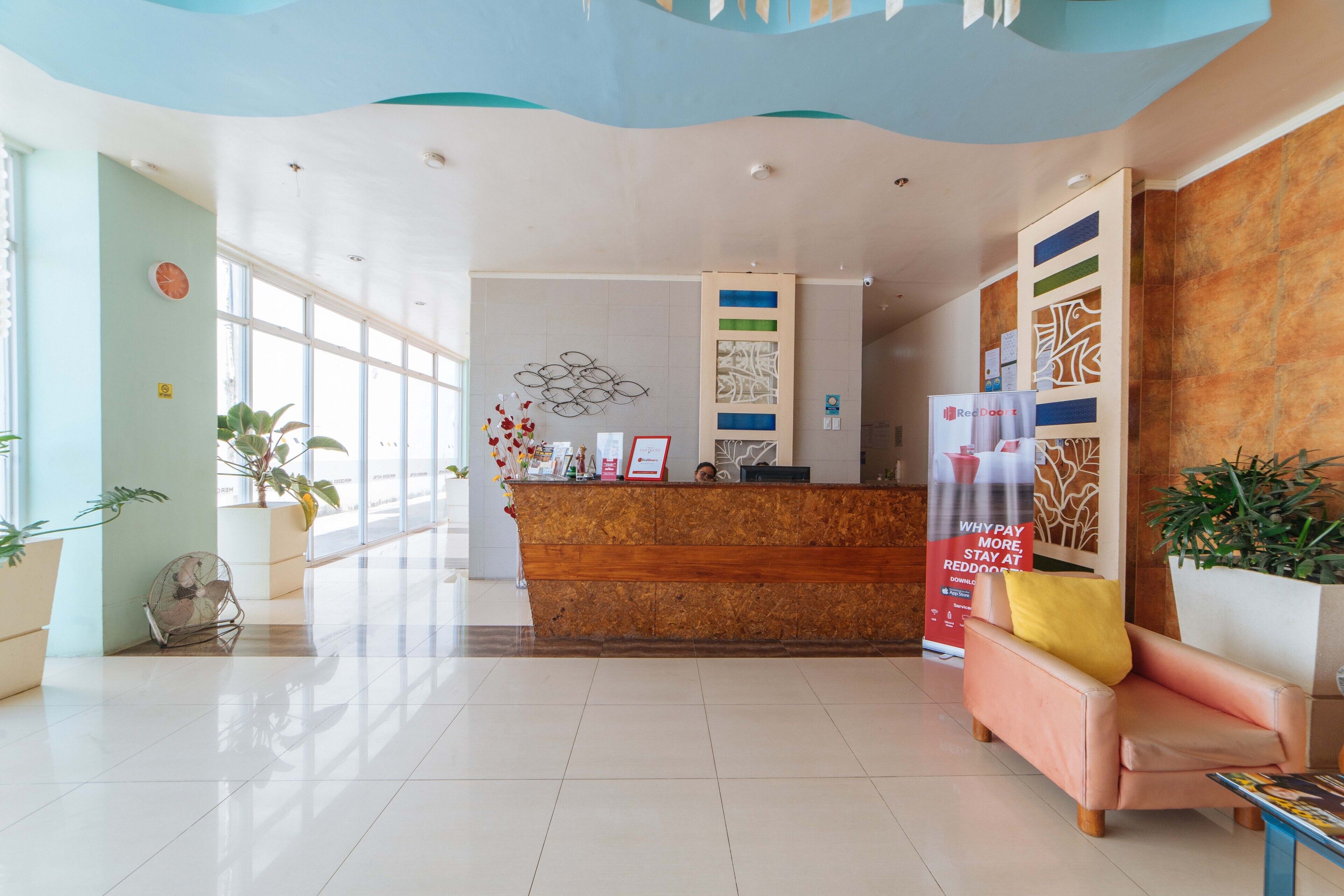 A reception area with a wooden reception desk, a seating area with a pink sofa, and potted plants.