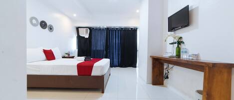 A modern hotel room with a bed, a wooden desk, a TV, and a bathroom with a shower curtain.