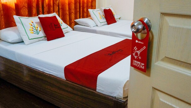 A hotel room with two beds, each with white bedding and red accents, including pillows and a red towel. A red sign on the door indicates the room is for 'Make Up'. - RedDoorz near Old Tagbilaran Airport (Tagbilaran)