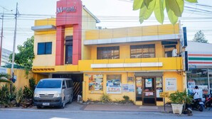 A two-story building with a red and yellow facade, a parked van, and various posters on the front. - RedDoorz near Old Tagbilaran Airport (Tagbilaran)