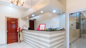 A reception area with a wooden door, a clock, a reception desk with a RedDoors sign, and a vase of flowers. - RedDoorz Premium @ Gabinete Road Palawan (Puerto Princesa)