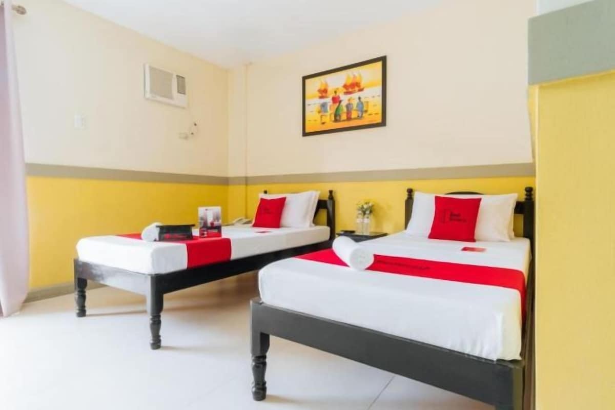 A hotel room with two beds, each with red and white bedding, a small bedside table, and a wall-mounted picture.