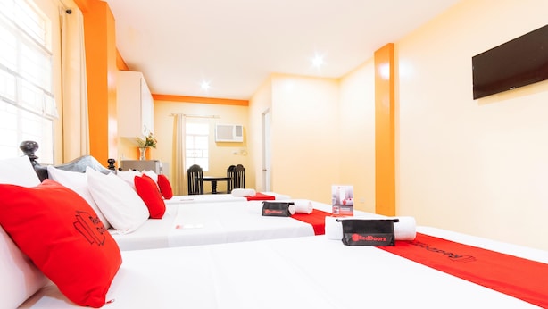 A hotel room with two beds, red and white bedding, a small table with a red towel, and a wall-mounted TV. - RedDoorz Premium @ Gabinete Road Palawan (Puerto Princesa)
