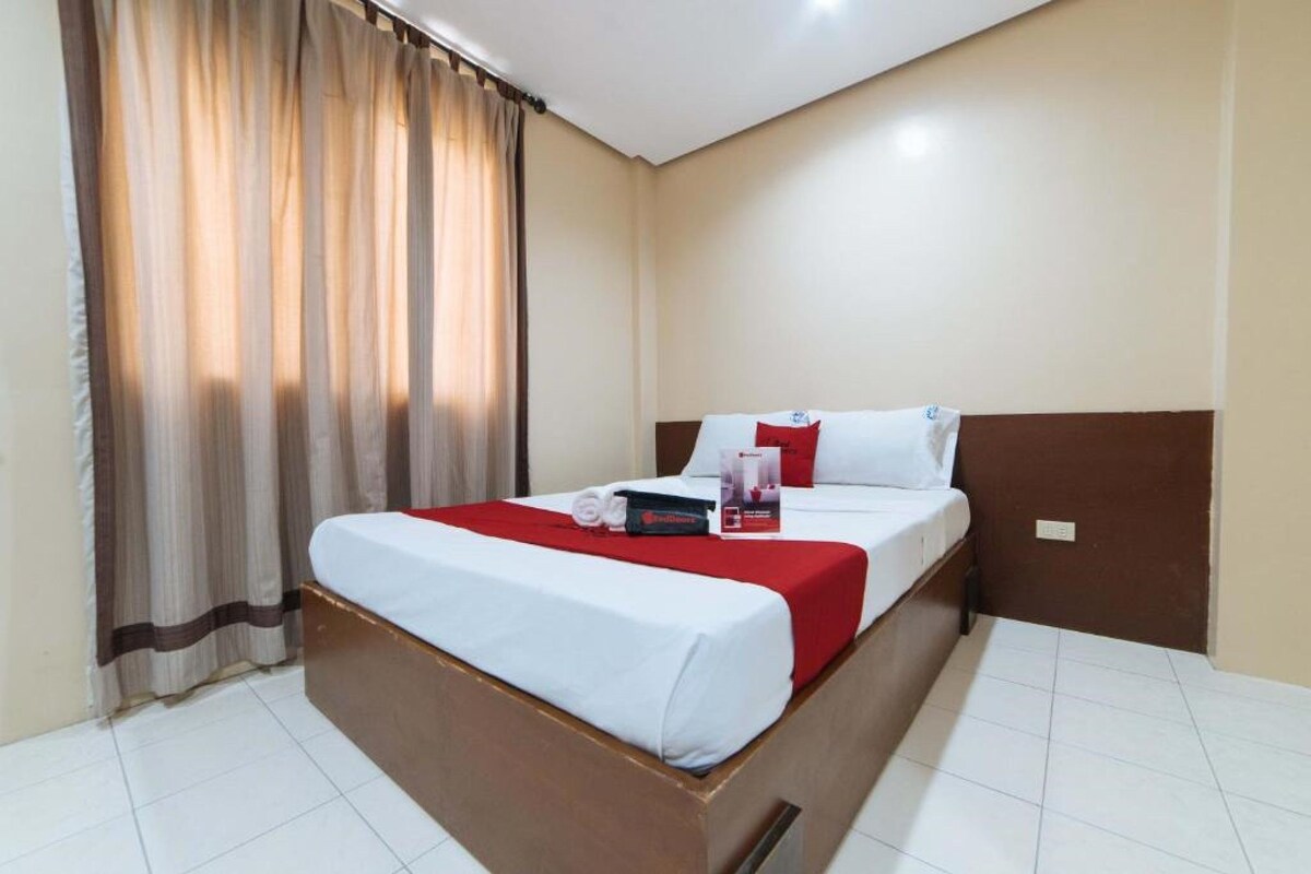 A hotel room with a bed, curtains, and a red and white bedspread.