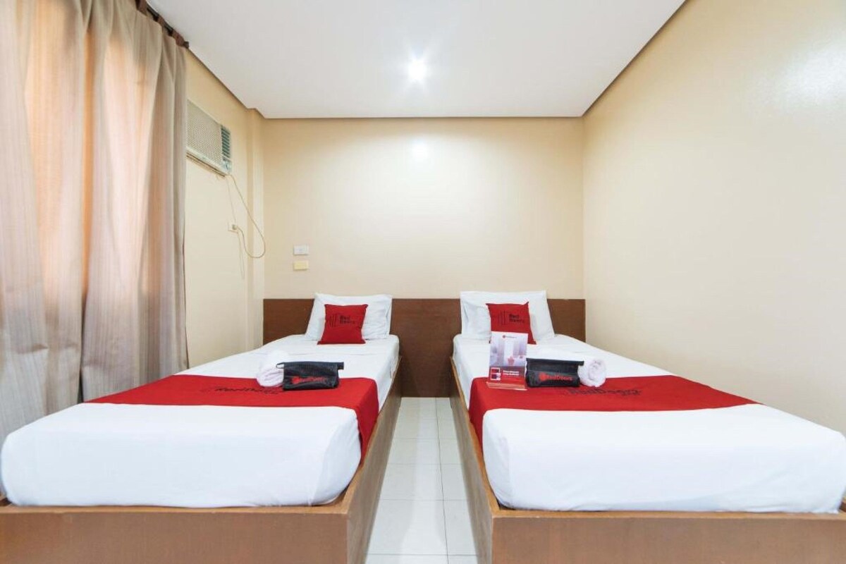 A hotel room with two single beds, each with a red blanket and white bedding.