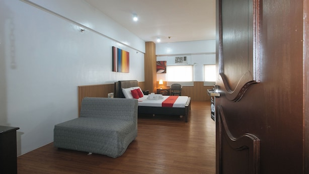 A hotel room with a bed, a grey armchair, a wooden headboard, a bedside table, a lamp, and a window with blinds. - RedDoorz near SM Manila (Manila)