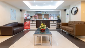 A reception area with a reception desk, two sofas, a coffee table with a floral arrangement, a map on the wall, and a clock. - RedDoorz near SM Manila (Manila)