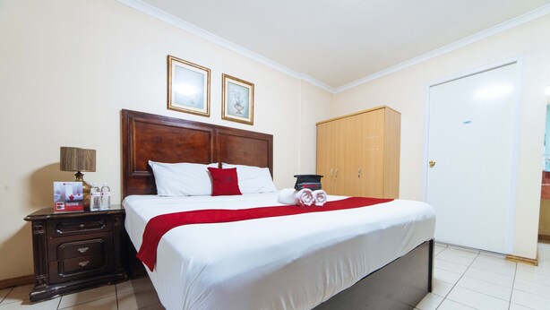 A hotel room with a large bed, wooden headboard, two framed pictures on the wall, a wardrobe, and a nightstand with a lamp and a coffee maker. - RedDoorz @ Clarkview 21st Street Angeles City (Angeles City)