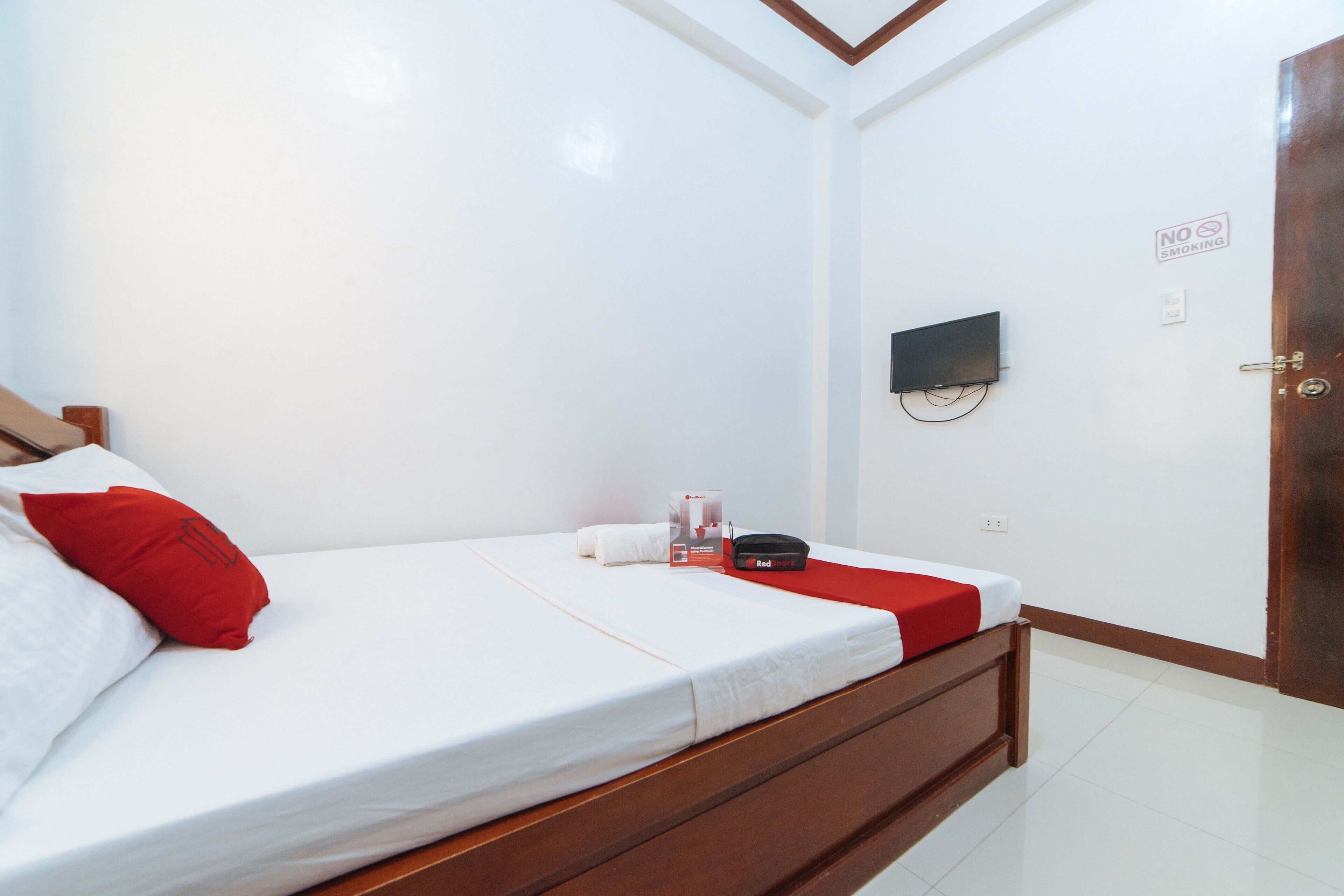 A hotel room with a bed, a TV mounted on the wall, and a door with a no smoking sign.