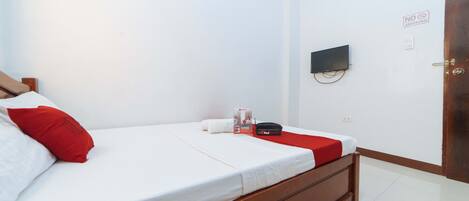 A hotel room with a bed, a TV mounted on the wall, and a door with a no smoking sign.