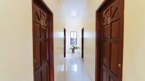A hallway with wooden doors, a potted plant, and a window at the end. - Reddoorz @ D Maagma Street - Vaccinated Staff (Kalibo)