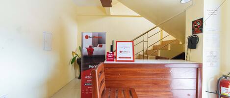 Un área de recepción con un banco de madera, un letrero de RedDoorz, una escalera y un extintor.