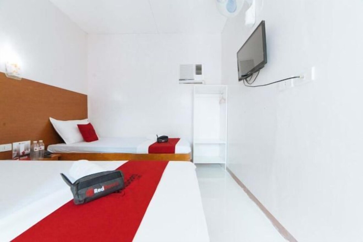 A hotel room with a bed, a TV mounted on the wall, and an air conditioning unit.