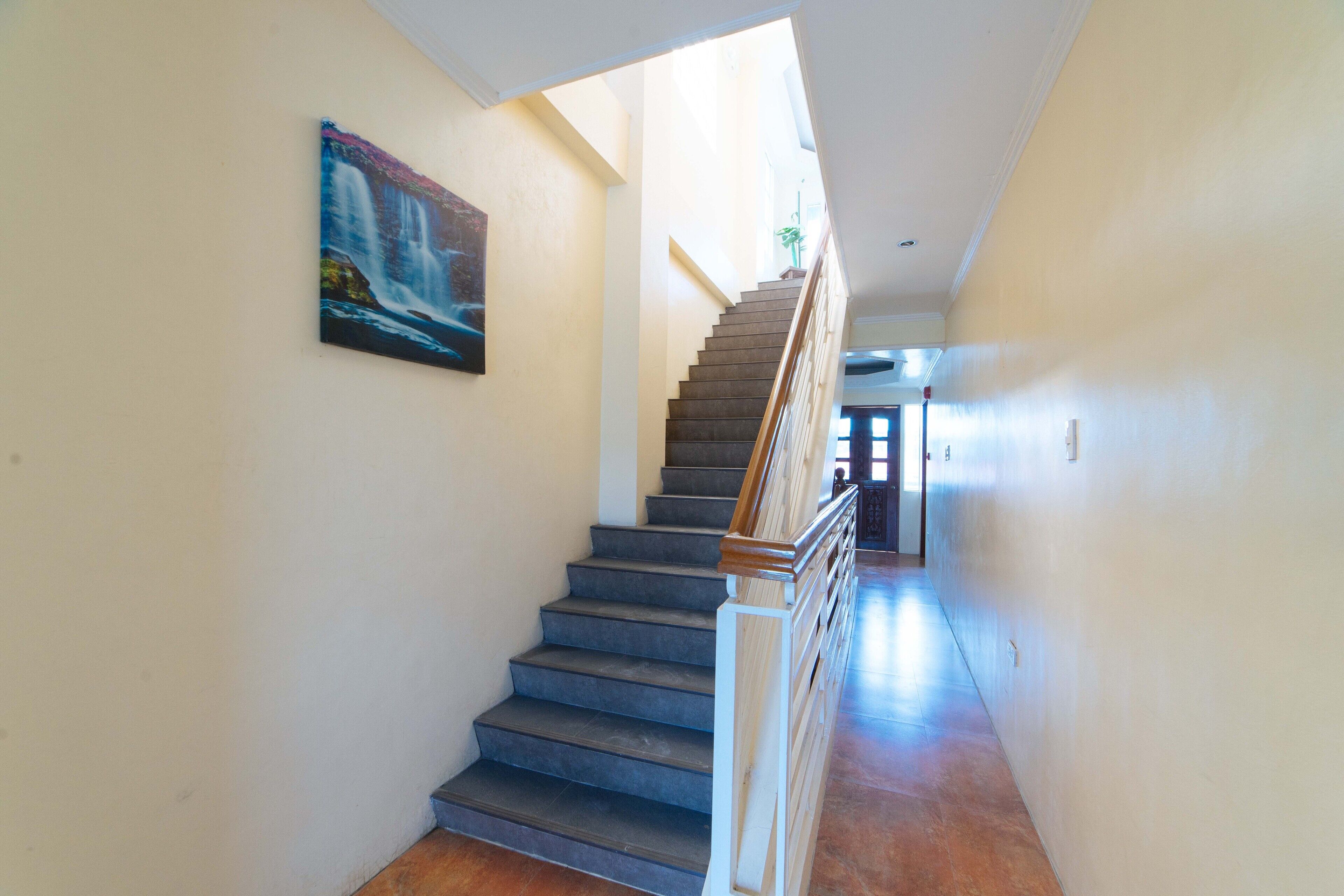 A staircase with a wooden handrail, a painting on the wall, and a view of the upper floor.