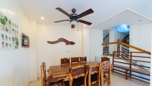 A dining area with a wooden table and chairs, a ceiling fan, and a staircase with wooden railings. - Reddoorz @ Old Buswang Road (Kalibo)