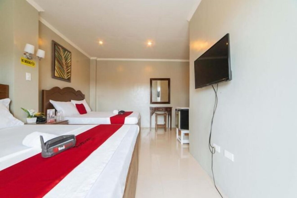 A hotel room with two beds, a desk, a chair, a flat-screen TV mounted on the wall, and a mirror.