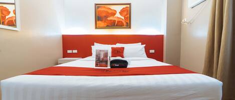 A hotel room with a bed, a red headboard, a framed artwork above the bed, and a window with curtains.